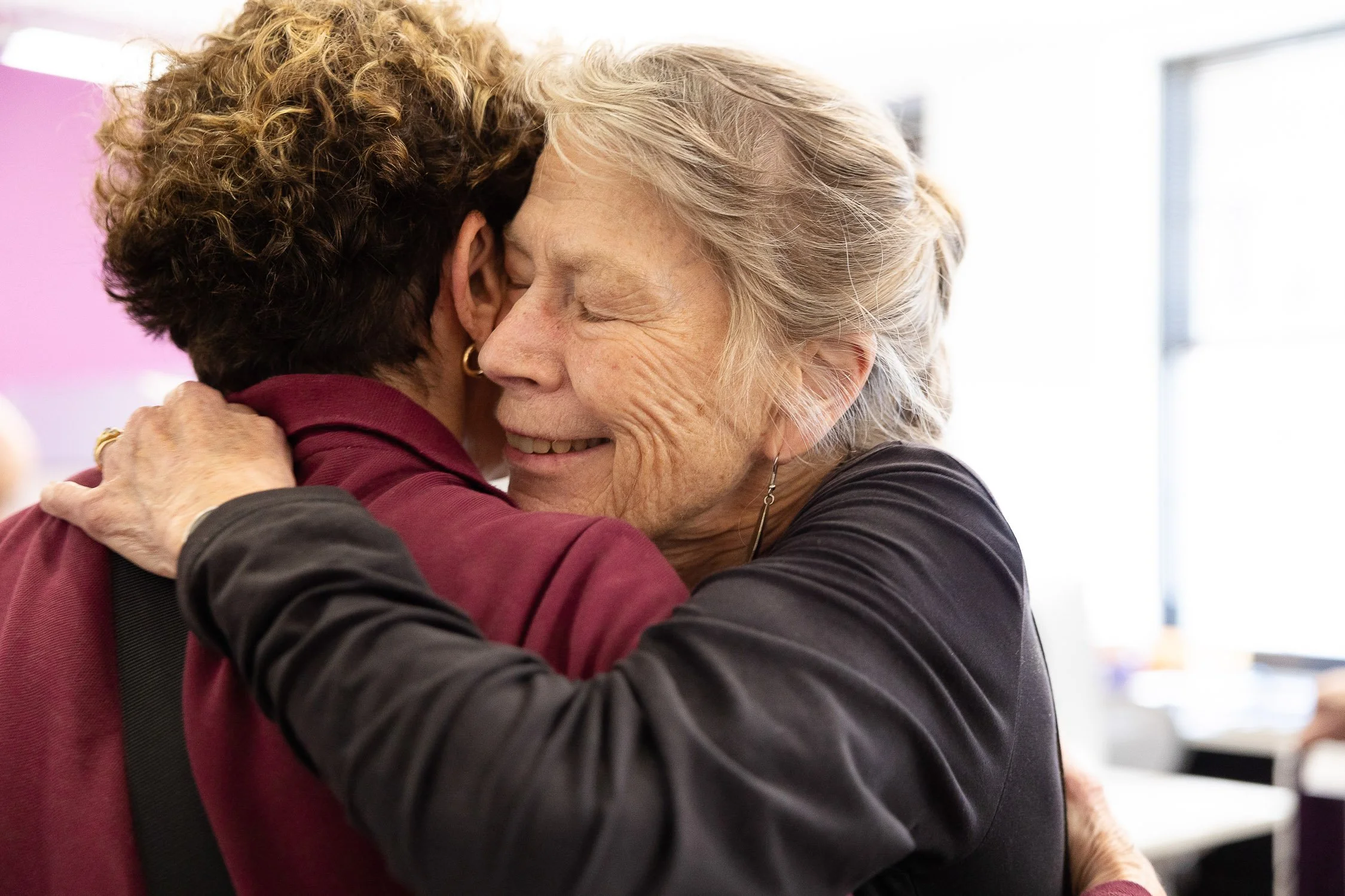 Two women smiling and embracing in a warm hug.