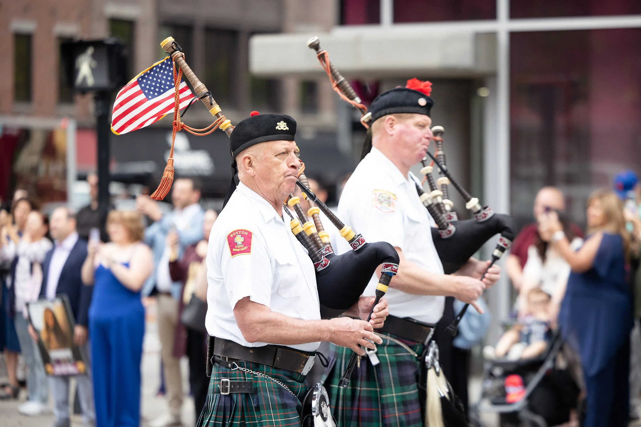 Two men in traditional Scottish attire playing bagpipes during a law school graduation procession in Boston.