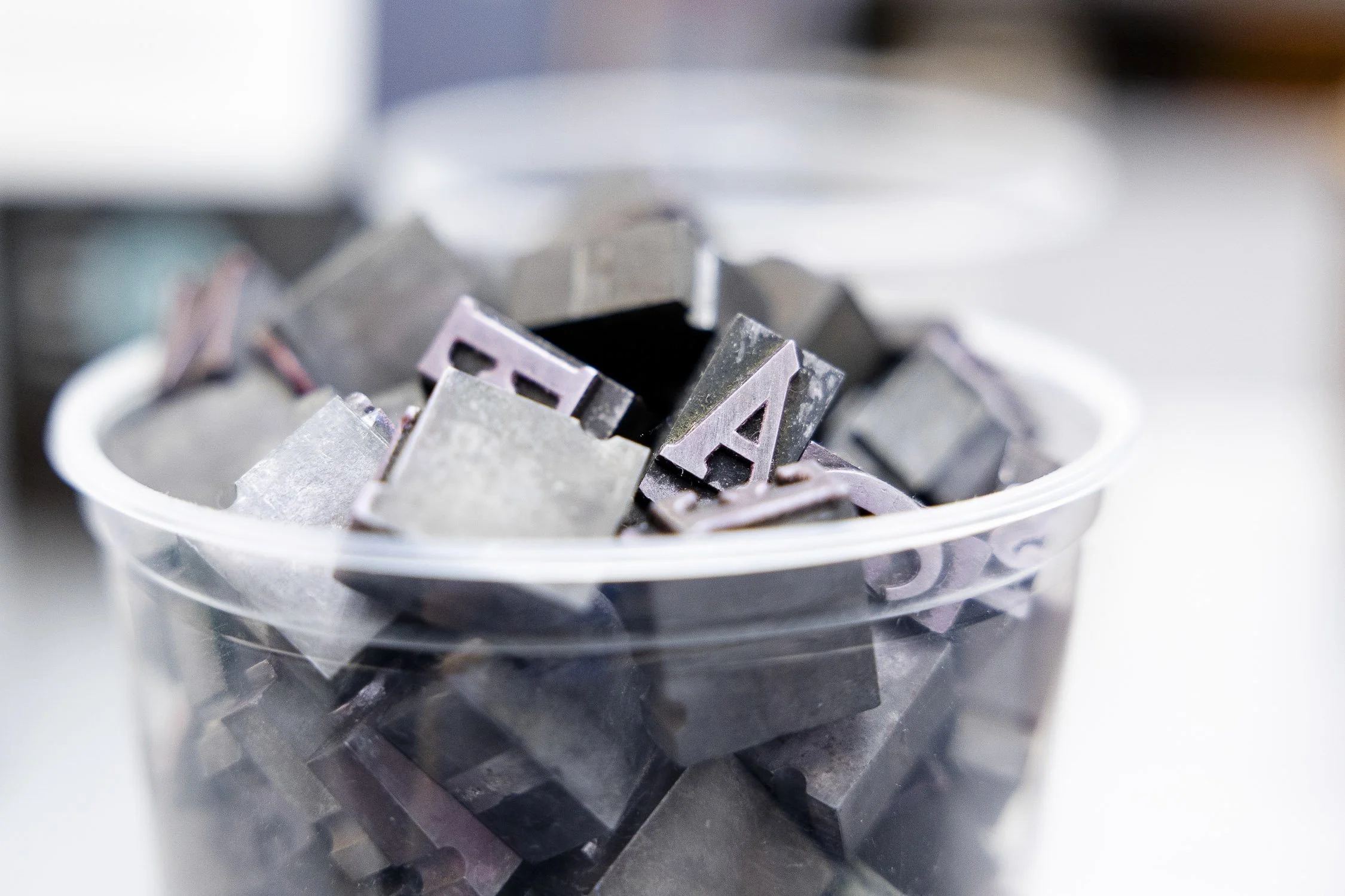 Close-up of a plastic container filled with vintage metal stamps with cut-out letters.
