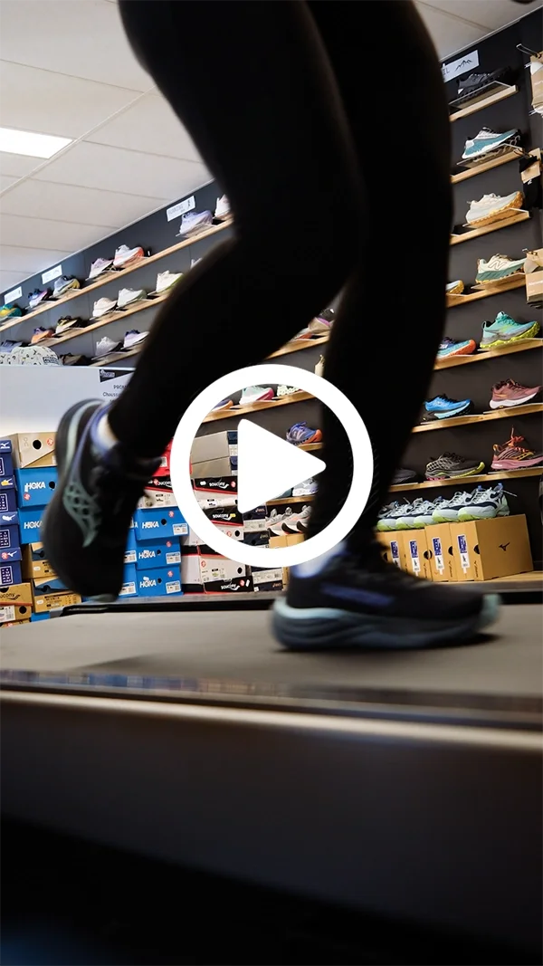 Vue en contre-plongée d'une personne en mouvement portant des chaussures de course, dans une boutique de chaussures avec étagères de sneakers en arrière-plan, lors d'une analyse de foulée avec Louis Gronemberger.