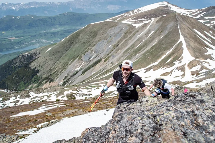 Louis Gronemberger, kiné et traileur, escalade une montagne enneigée avec un paysage de montagnes et de vallées en arrière-plan, lors de la SkyRace de Matheysins.