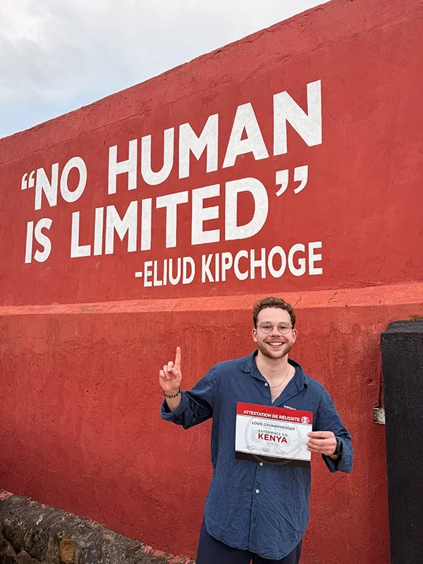 Louis Gronemberger, jeune homme souriant avec des lunettes, tenant un certificat, faisant un geste de la main devant un mur rouge avec une citation d'Eliud Kipchoge : "Aucun humain n'est limité".