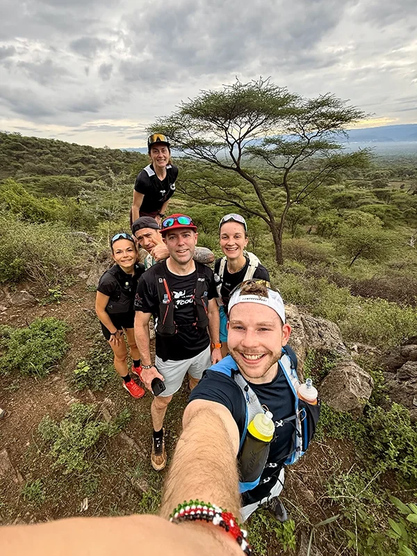 Groupe de sept traileurs posant pour une photo en pleine nature, avec un arbre au fond et un ciel nuageux, dans la région d'Iten au Kenya.