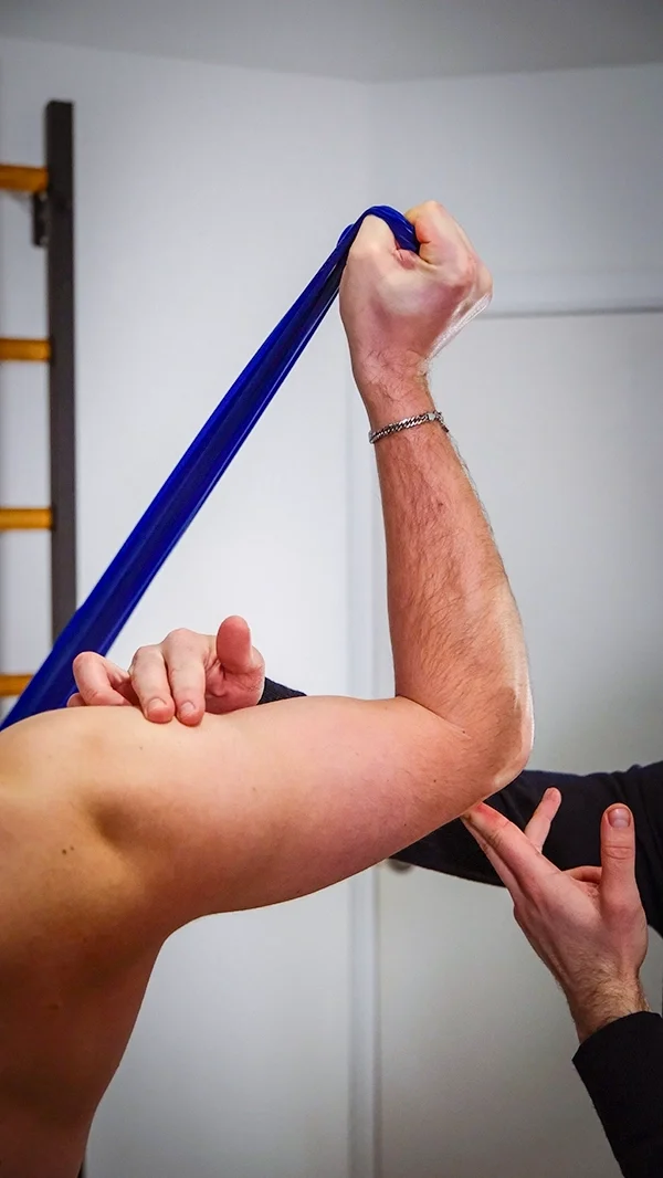 Un homme soulevant un élastique d'exercice bleu avec son biceps, une autre personne mesure la force de son bras.