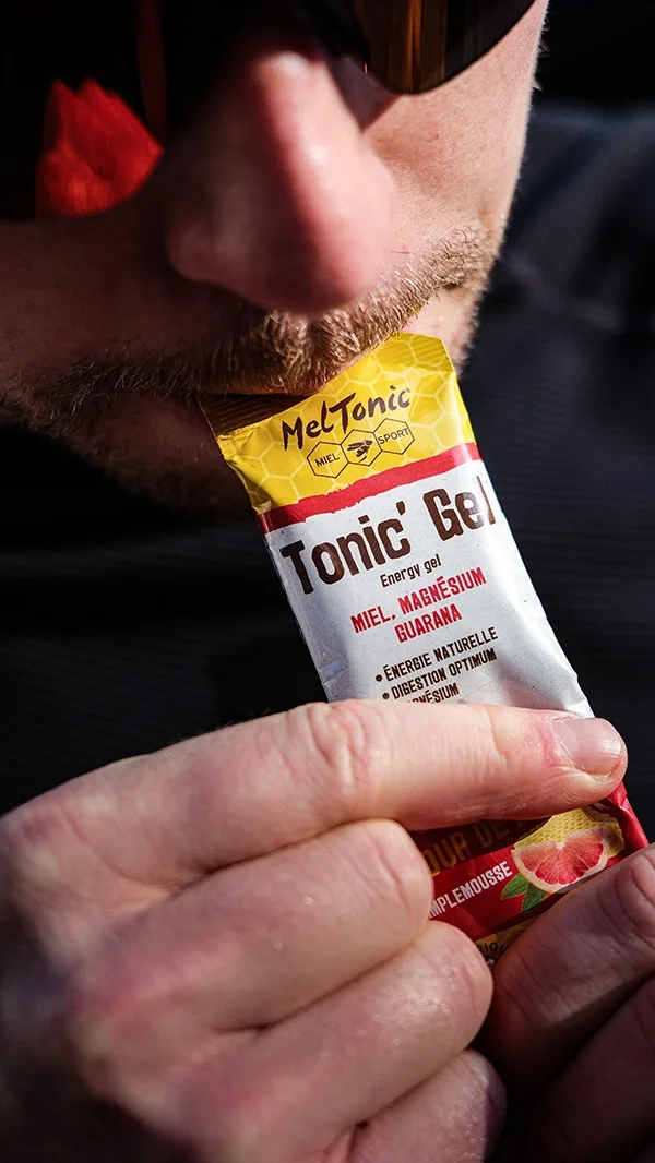 Louis Gronemberger tenant un gel énergétique MelTonic, près de sa bouche, avec un focus sur le produit.