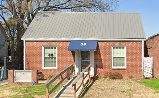 Brick house with a metal roof, front entrance with a blue awning, wheelchair-accessible ramp, and two front windows.