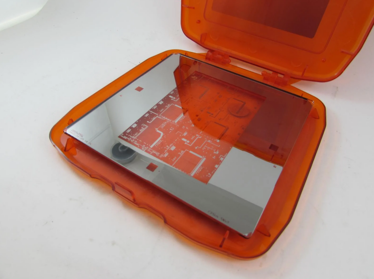 A handheld mirror with an orange plastic case, reflecting pathways and rooms of a building.