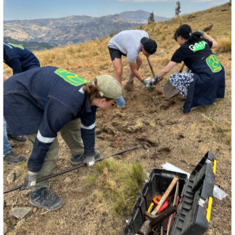 Group of volunteers planting trees on a hillside with mountains in the background.