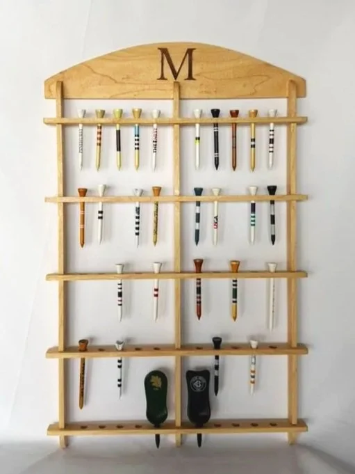 Wooden wall rack with multiple shelves holding golf tees and two golf divot repair tools.