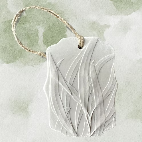 White ceramic tag with leaf pattern and a jute string. Botanical Bas Relief Essential Oil Diffuser.