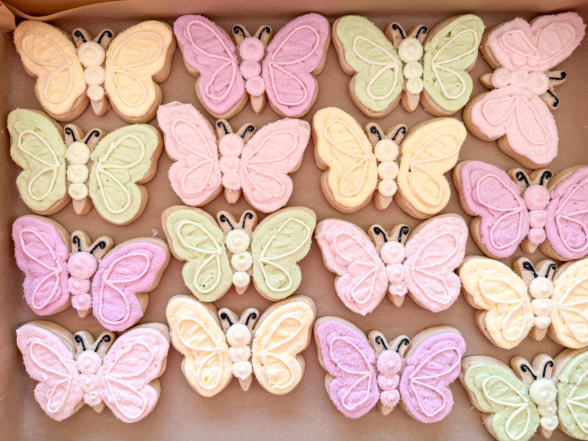 Colorful butterfly-shaped sugar cookies decorated with pastel pink, yellow, and green icing, arranged on a tray.