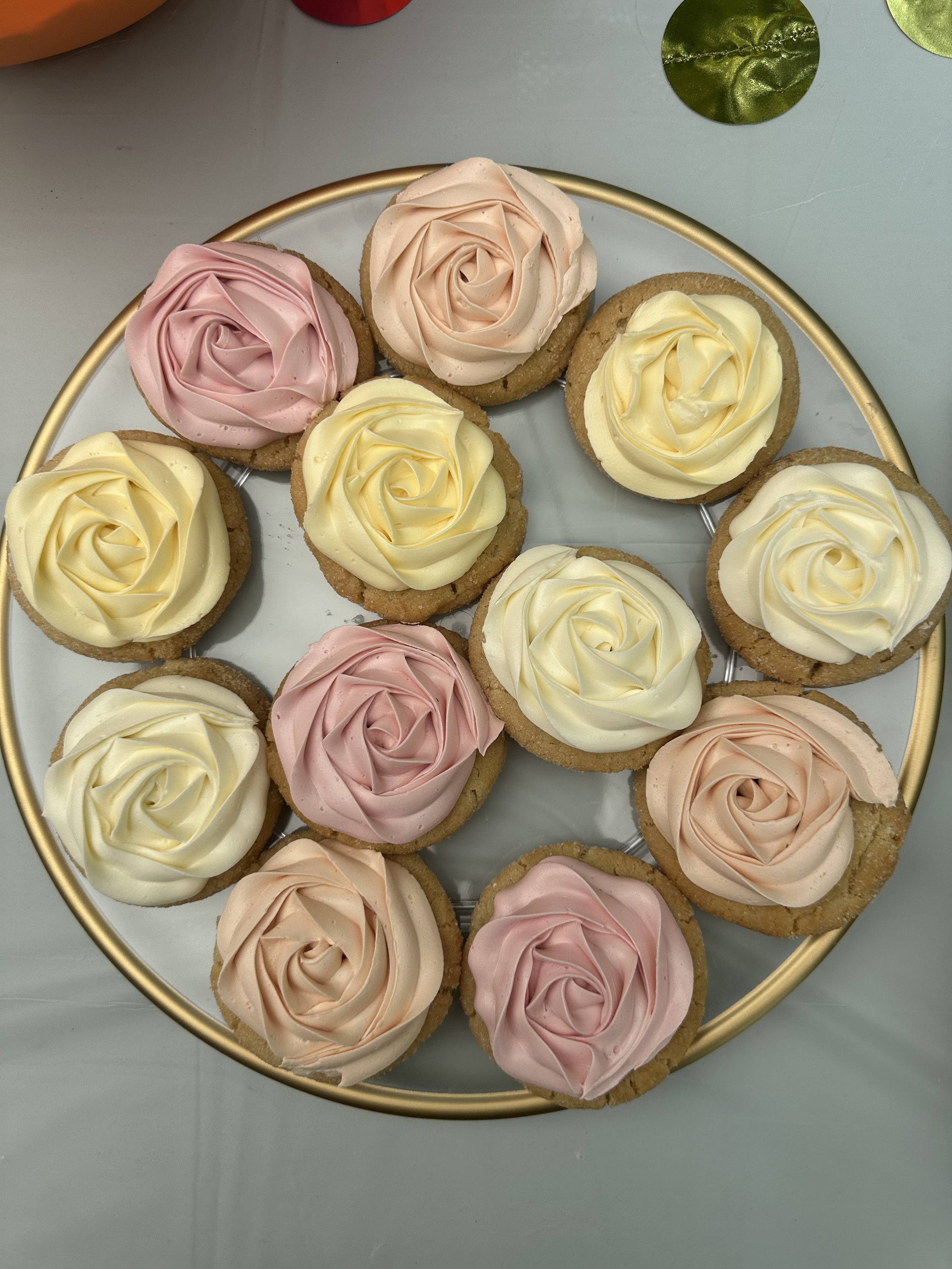 Assorted cupcakes with rose-shaped frosting in pink, yellow, and cream colors on a circular gold tray.