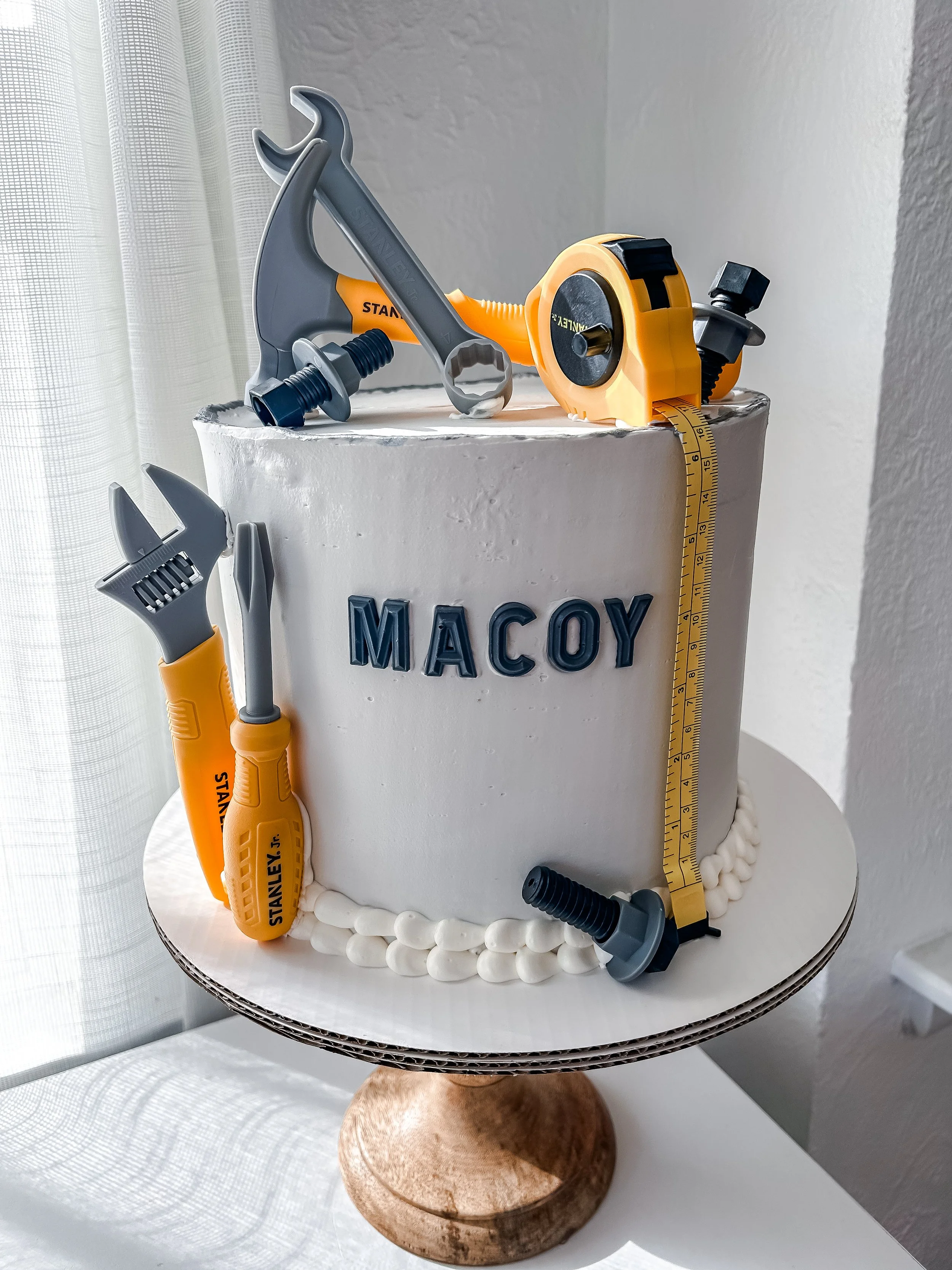A cake decorated with toy tools and the word 'MACOY' on it, resembling a construction theme.