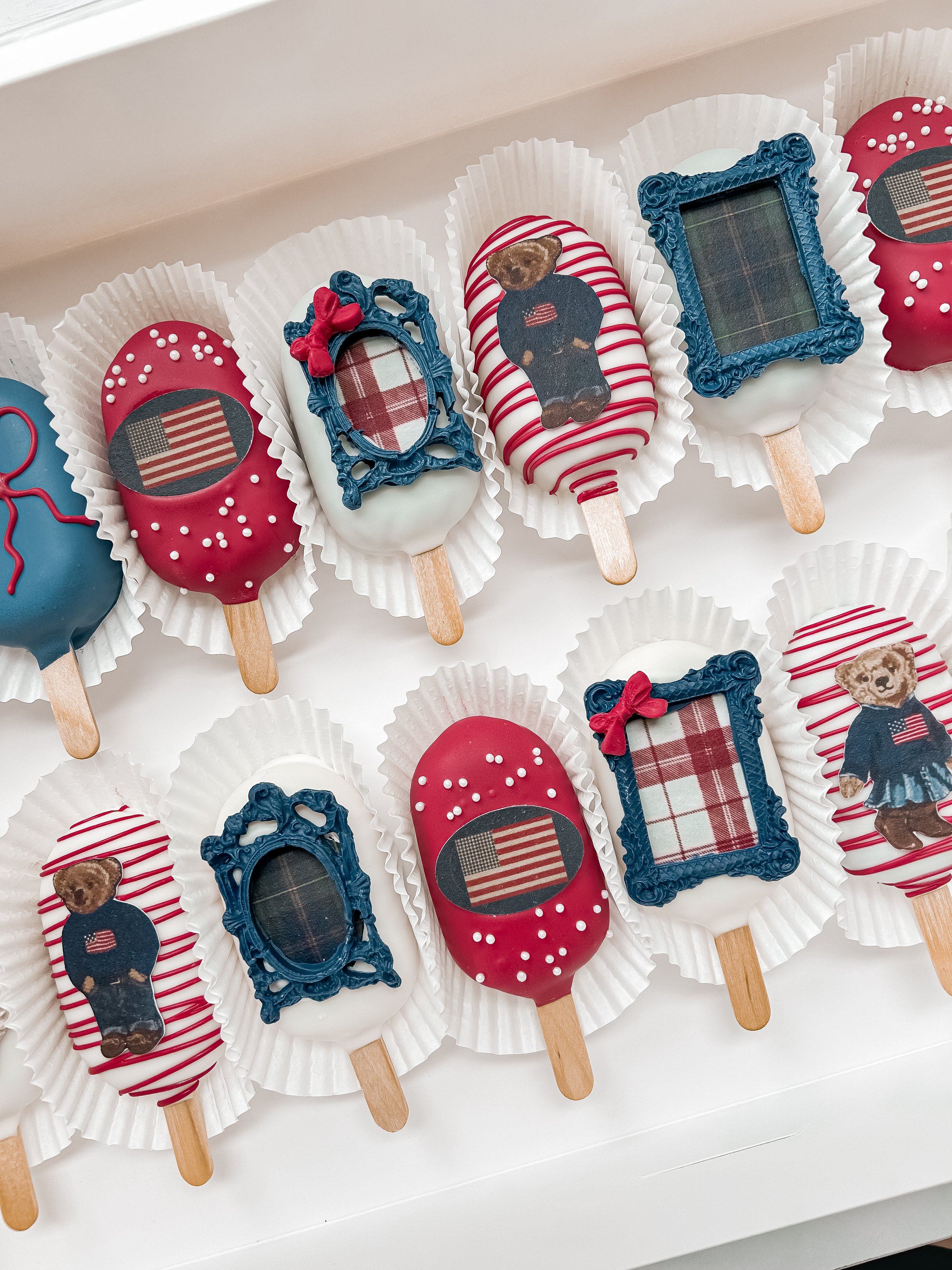 Patriotic themed ice cream bars decorated with American flags, teddy bears, and frames, arranged on a white surface with white paper liners.