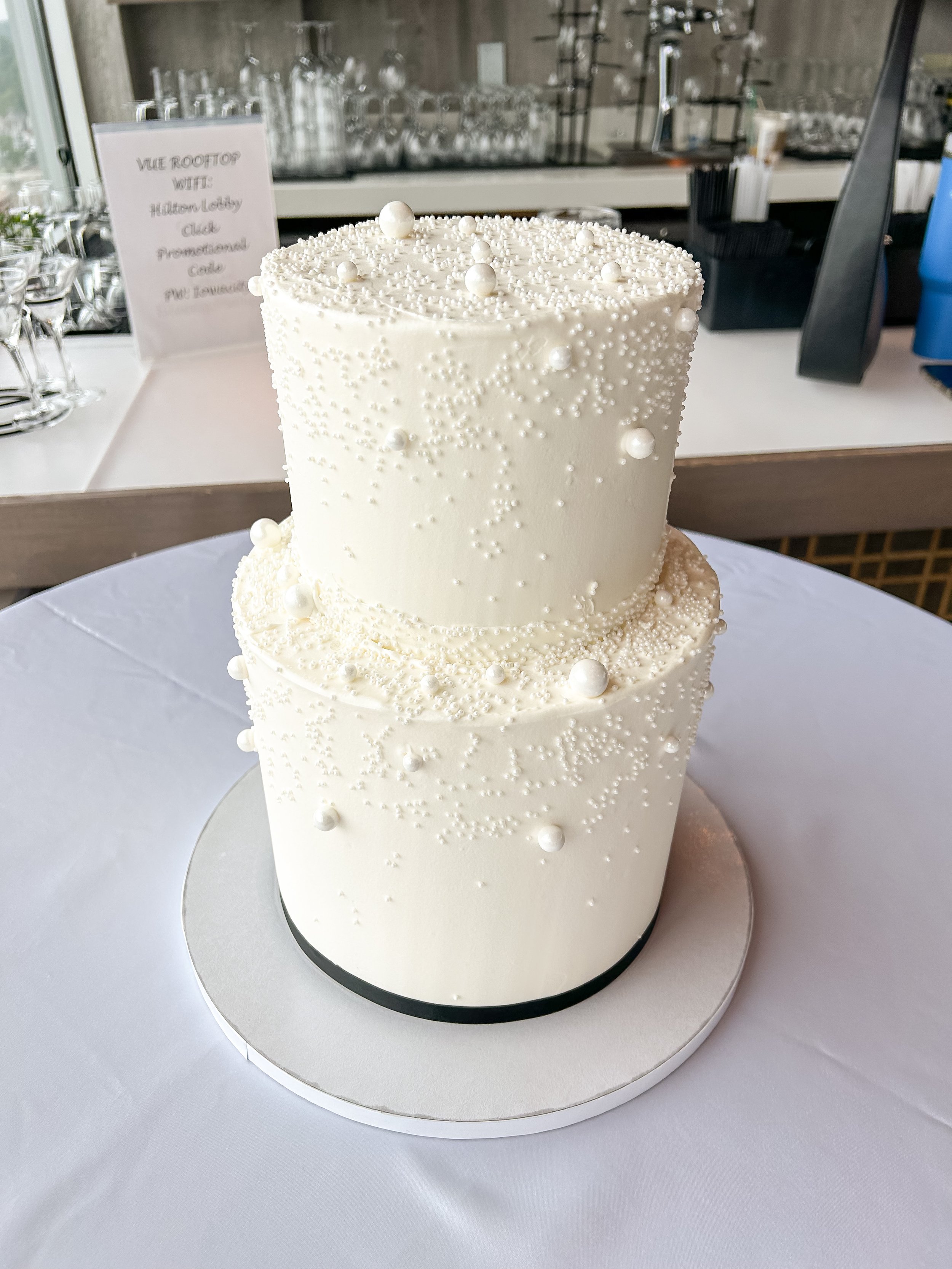 Two-tiered white wedding cake decorated with small pearl-like and bead-like embellishments.