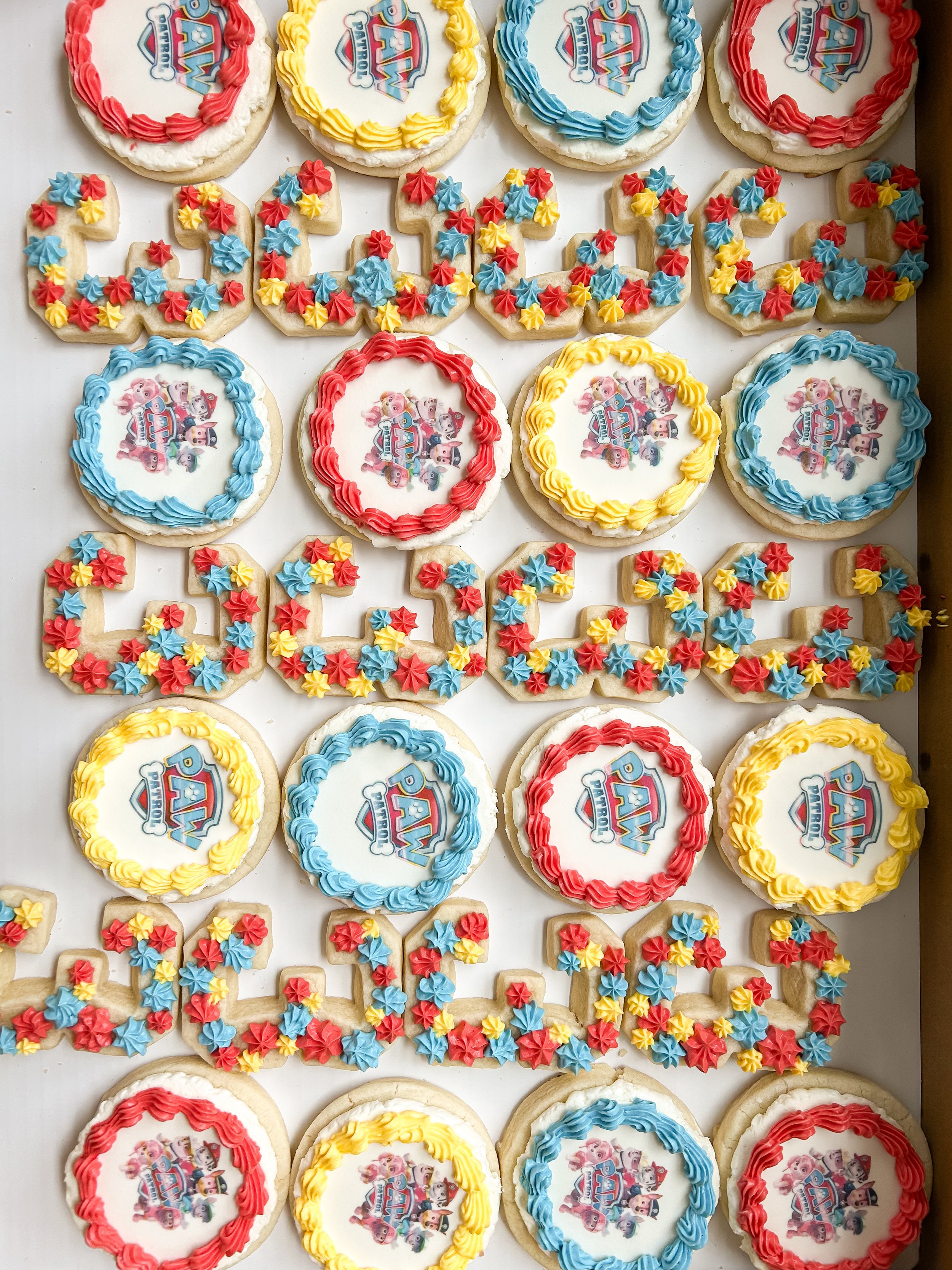 Decorated cookies and cupcakes themed birthday celebration with 'PAW Patrol' characters, featuring red, yellow, and blue icing.