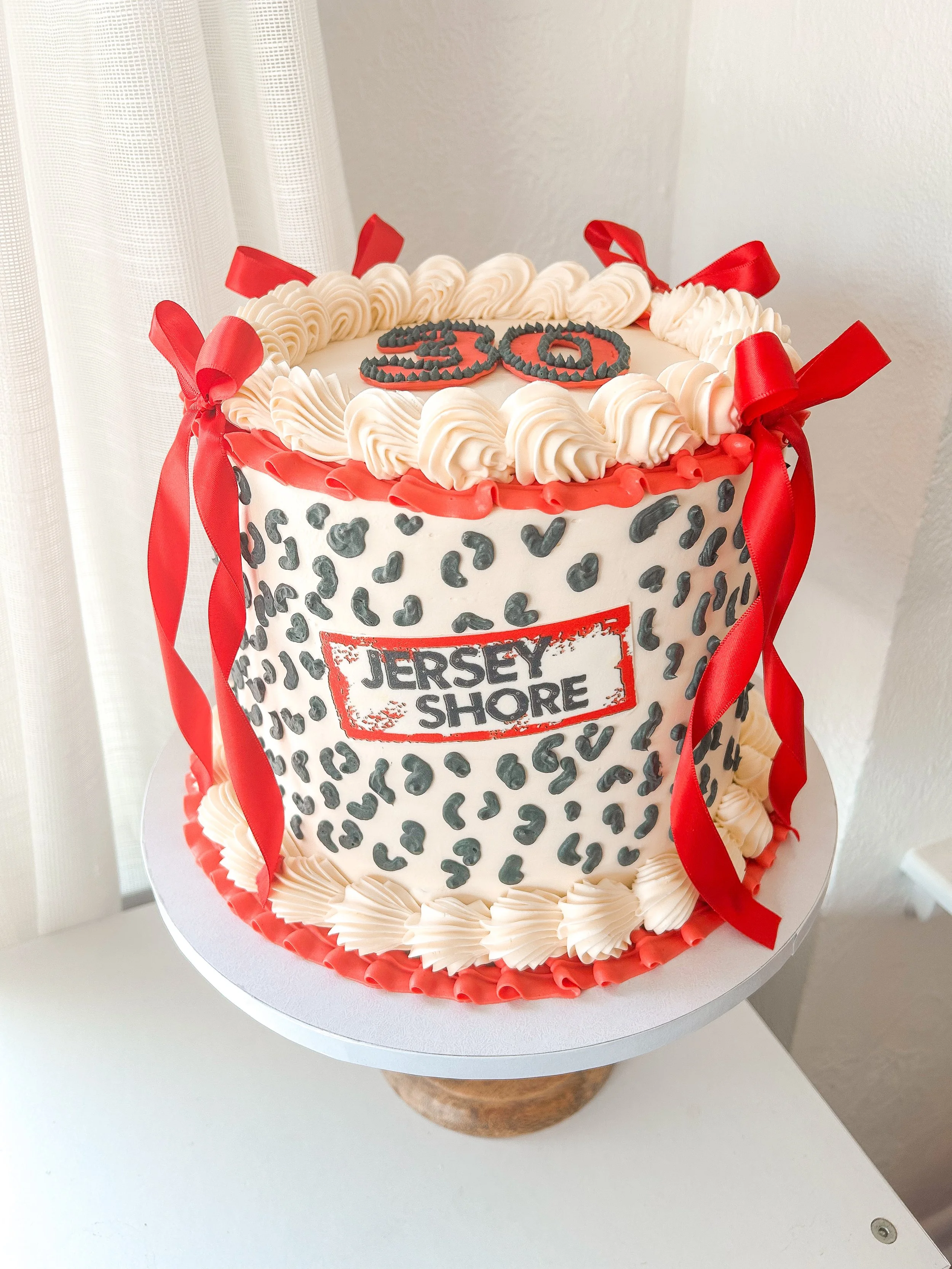 A cake with a Jersey Shore theme, decorated with a leopard print pattern, red ribbons, and topped with piping and the number '13' in black icing.