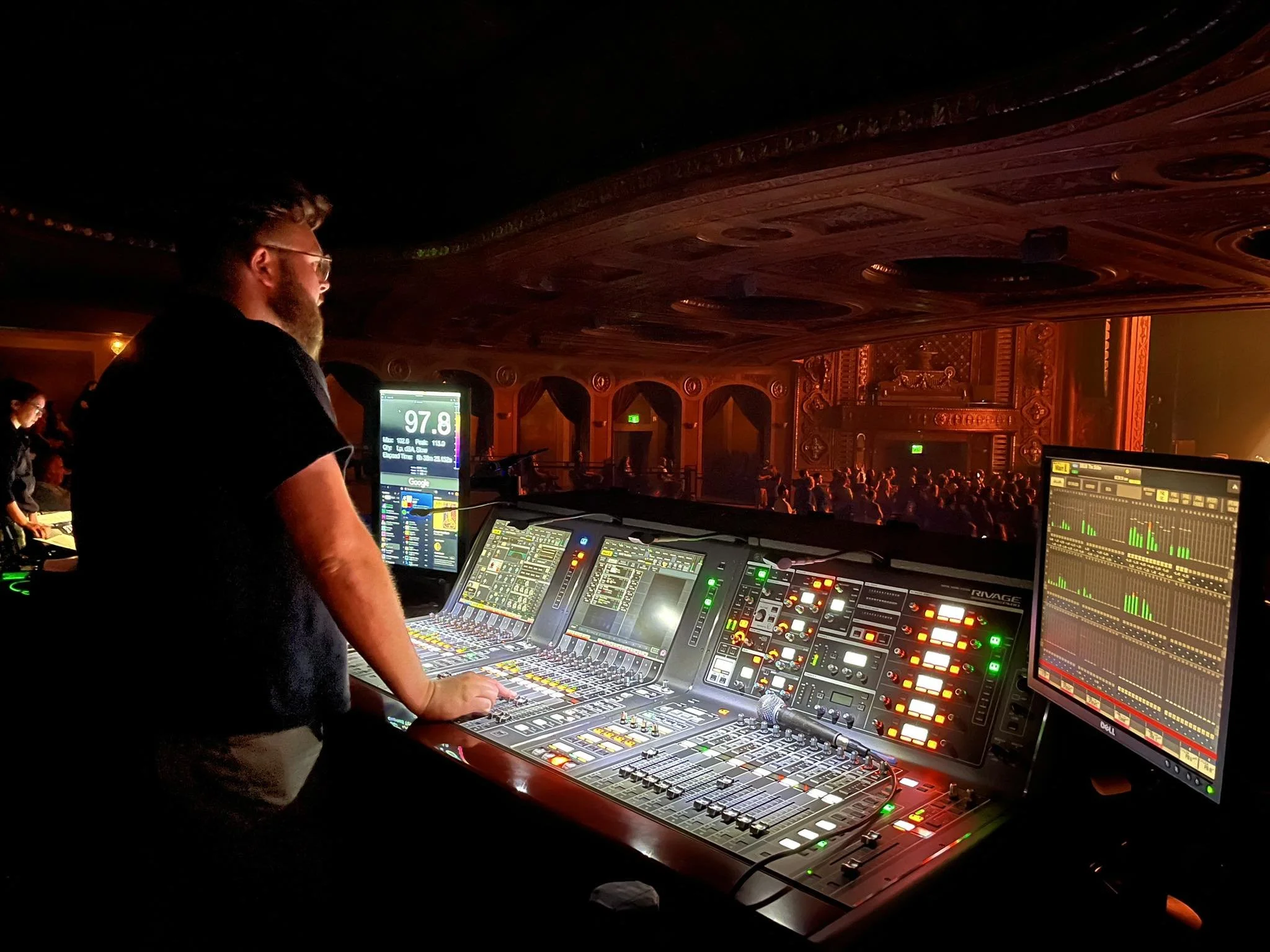 Hunter Shaw mixing FOH at the Paramount Theater in Seattle with a large crowd in the background, illuminated by vibrant lights, and audio equipment in the foreground.