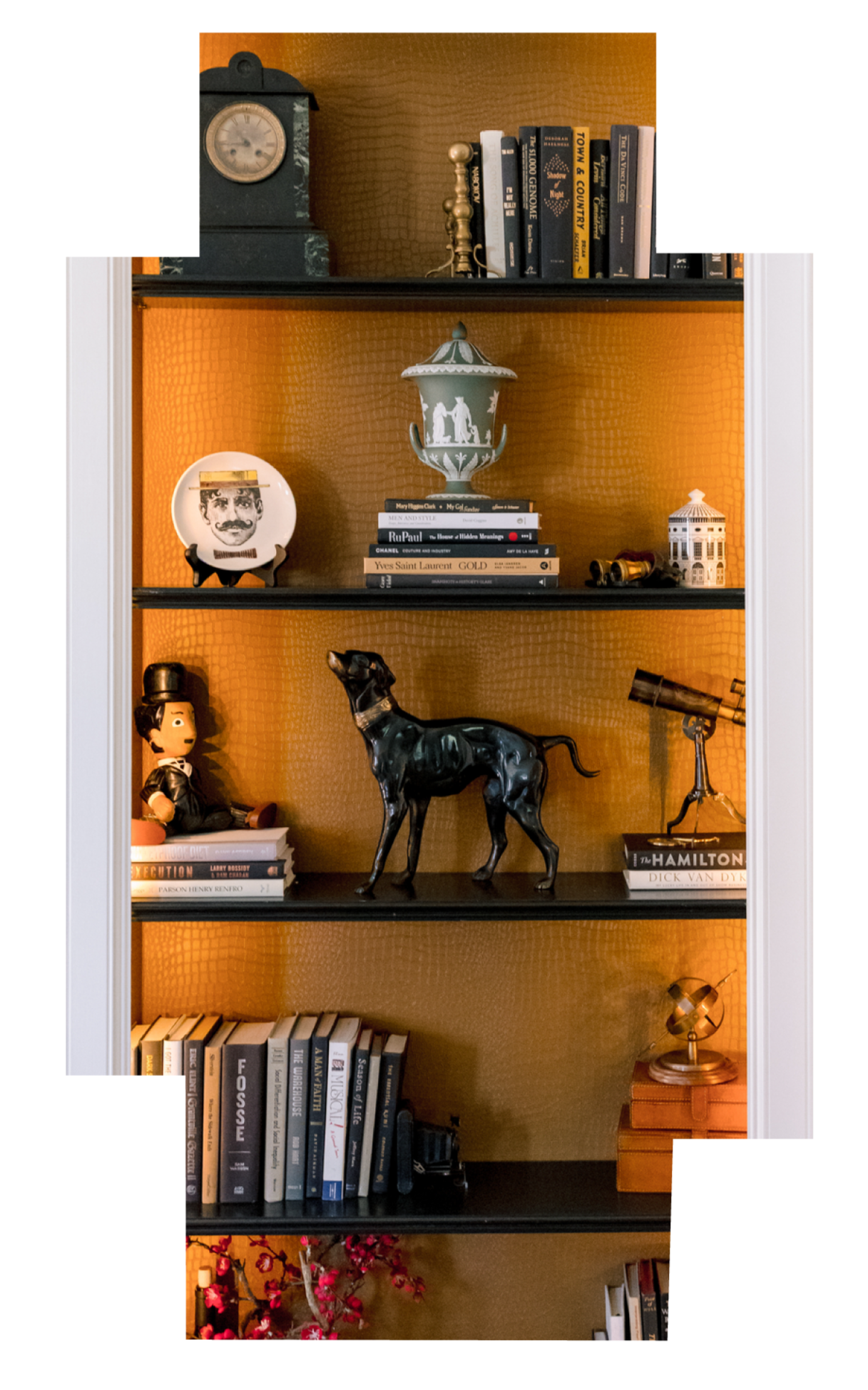 Bookshelf with decorative items including a clock, books, a small doll, a black dog sculpture, a telescope, and various knickknacks against an orange background.