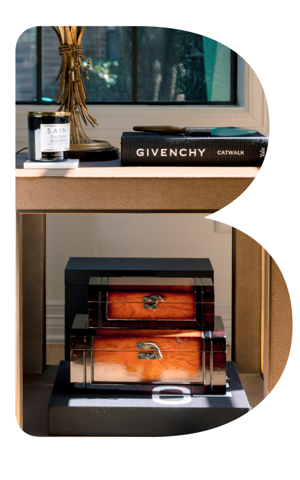 Decorative home decor items on a table, including a black candle, a brass sculpture resembling a tree, a Givenchy Catwalk book, and a turquoise tool, with two wooden boxes on the shelves below.