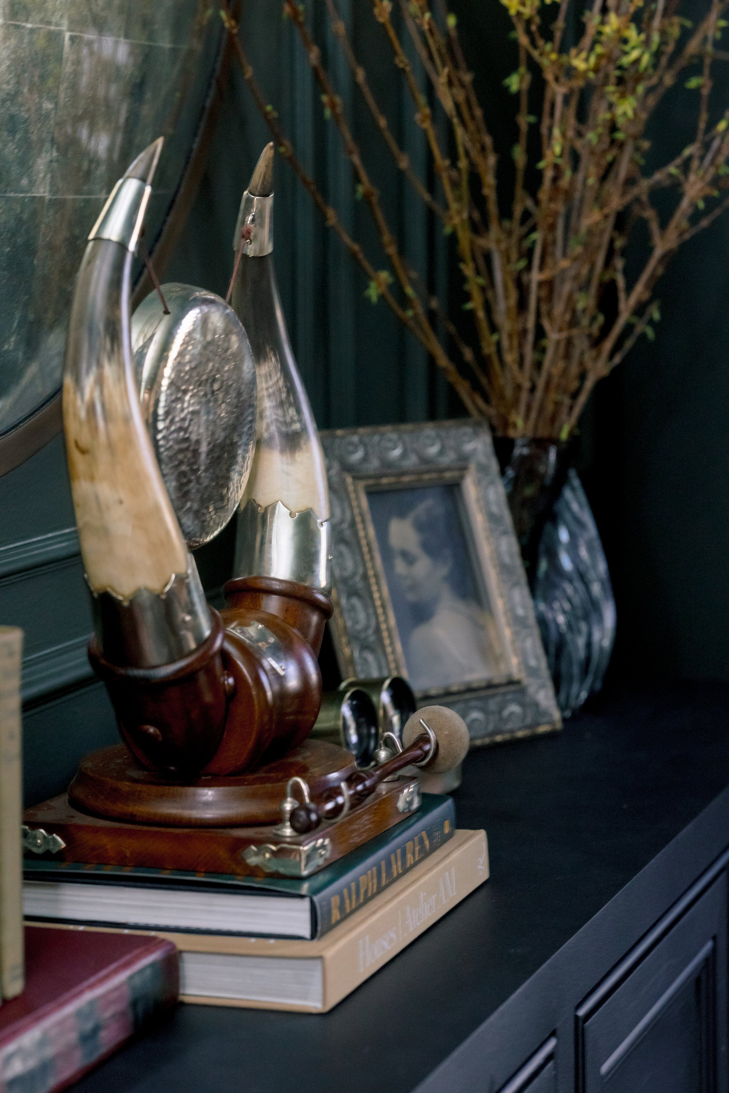 Decorative tabletop with framed photo, books, a wooden sculpture, and a tall vase with bare branches.