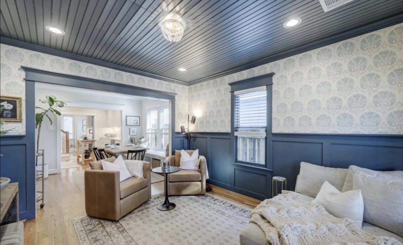 Living room with blue and white walls, wooden floors, beige and white sofas, and a small black round table.