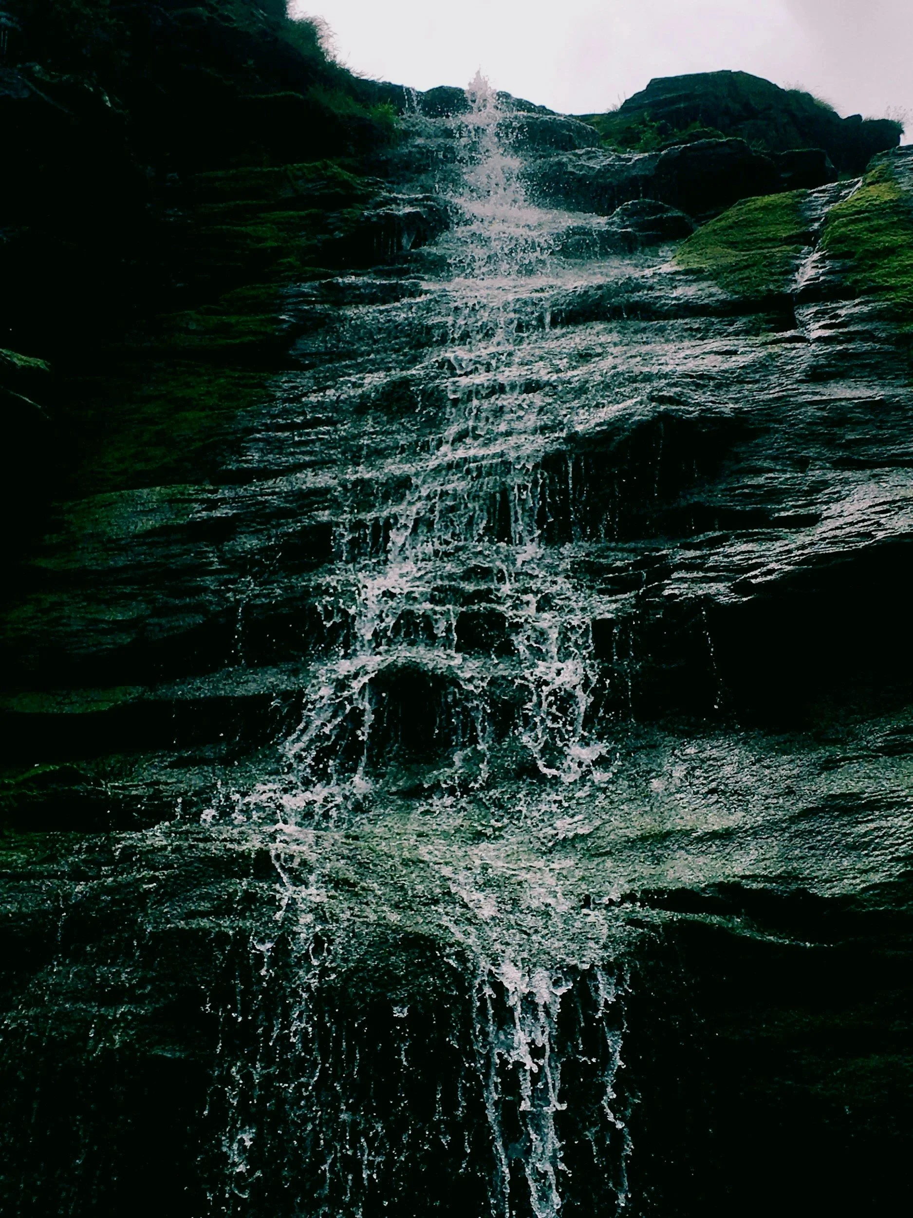A waterfall with water running down jagged rocks, with slight mossy greenery on some of the rocks.
