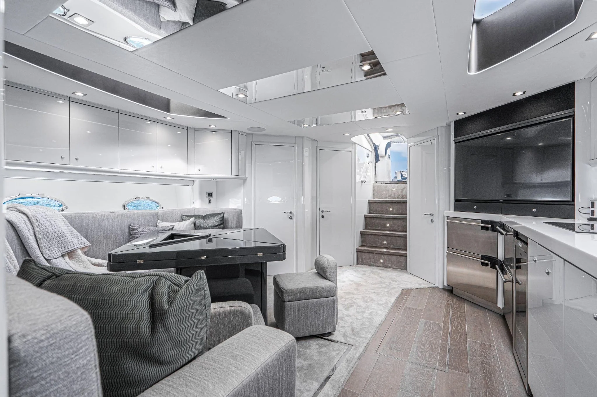 Interior of a luxurious yacht with white cabinetry, a staircase, a large flat-screen TV, a grand piano, and comfortable seating.