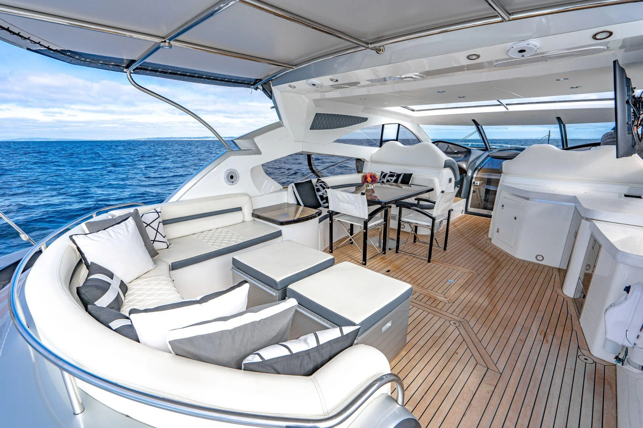 Luxury yacht deck with white seating, black and white cushions, a dining table with flowers, and a view of the ocean in the background.