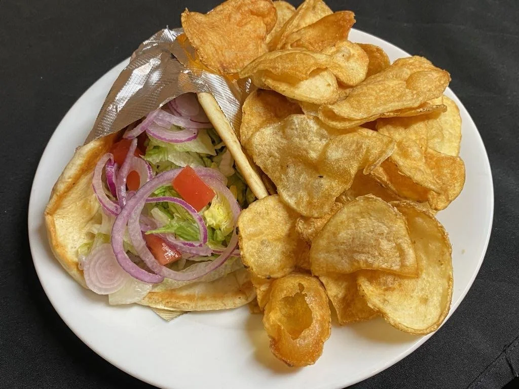 A plate of potato chips and a hot dog with lettuce, onions, tomato, and mustard in a bun.