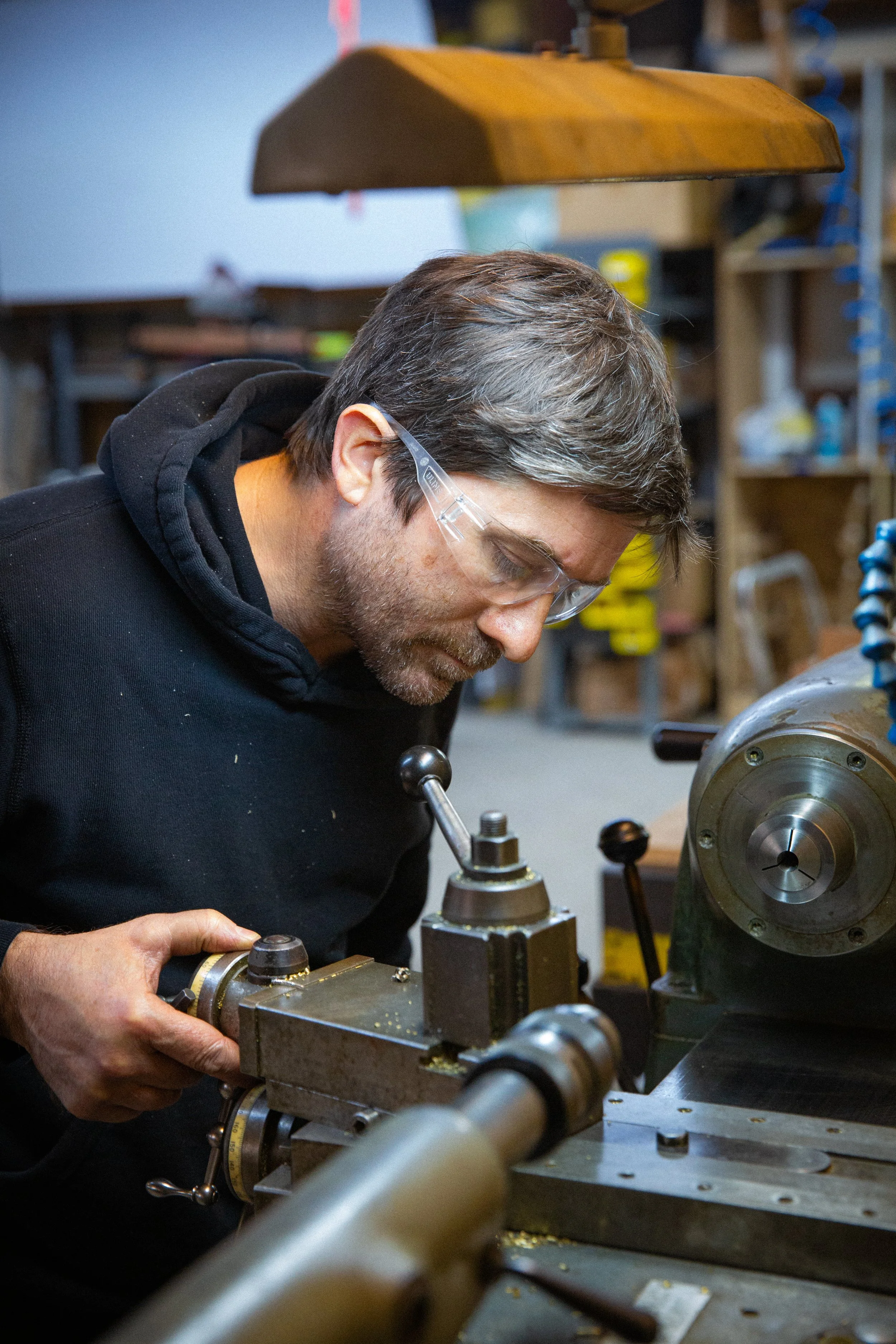 Brightbound Lighting partner, Will Kavesh, wearing safety glasses working on a metal lathe in a workshop.