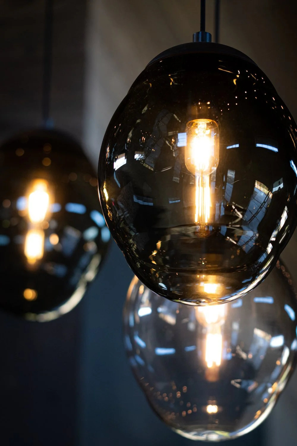 Close-up of modern glass pendant lights with filament bulbs, reflecting surrounding windows and environment.