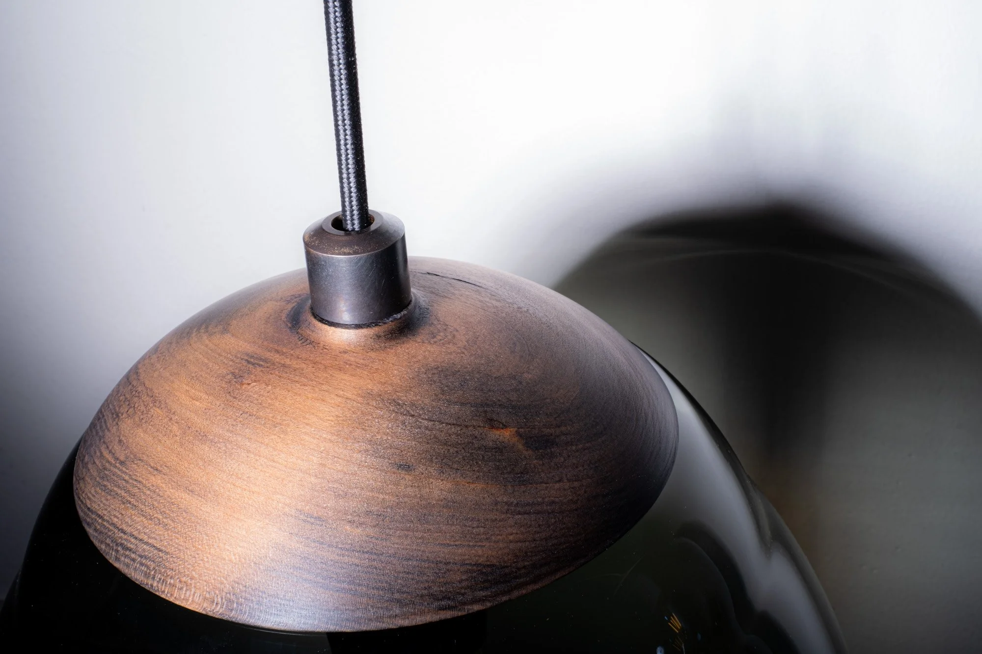 Close-up of a hanging pendant lamp with a black and brown wood-textured shade and black cord against a plain wall.