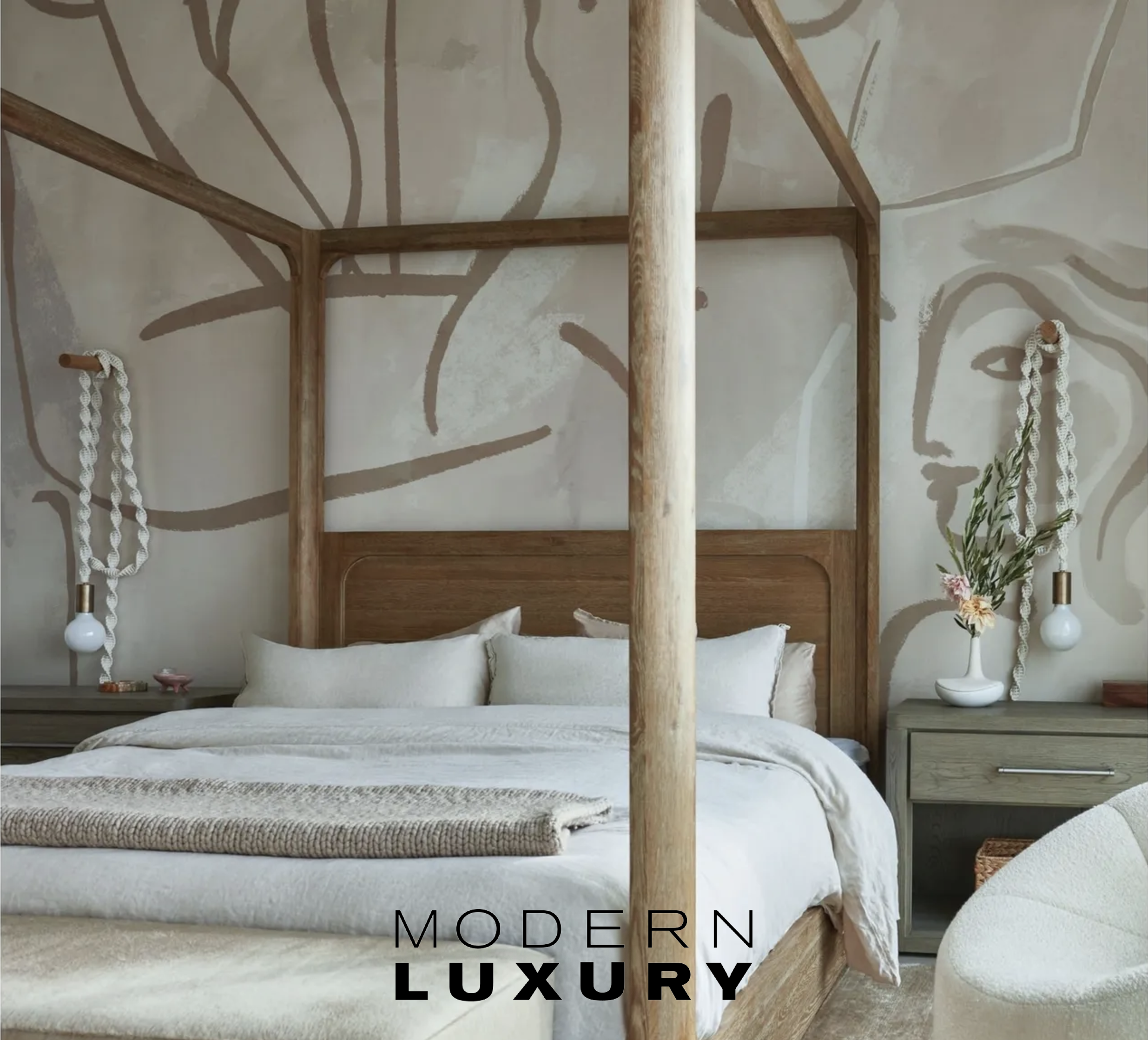 A modern bedroom with a four-poster bed, white bedding, and a carved wooden headboard. Light gray nightstands with decorative items, hanging lamps with exposed bulbs, and a wall mural with abstract line art of a face in neutral tones.