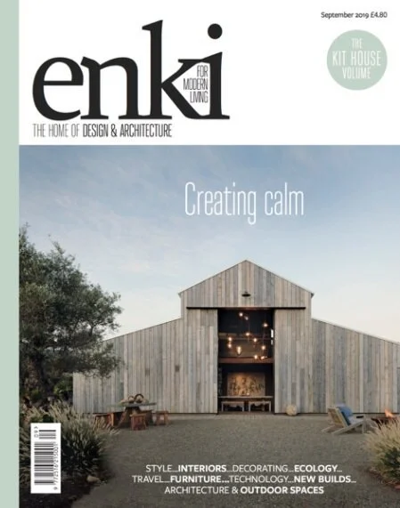 Magazine cover of 'ENKI' featuring a modern wooden barn with an open front, situated in a natural landscape with trees, and the headline 'Creating calm'.