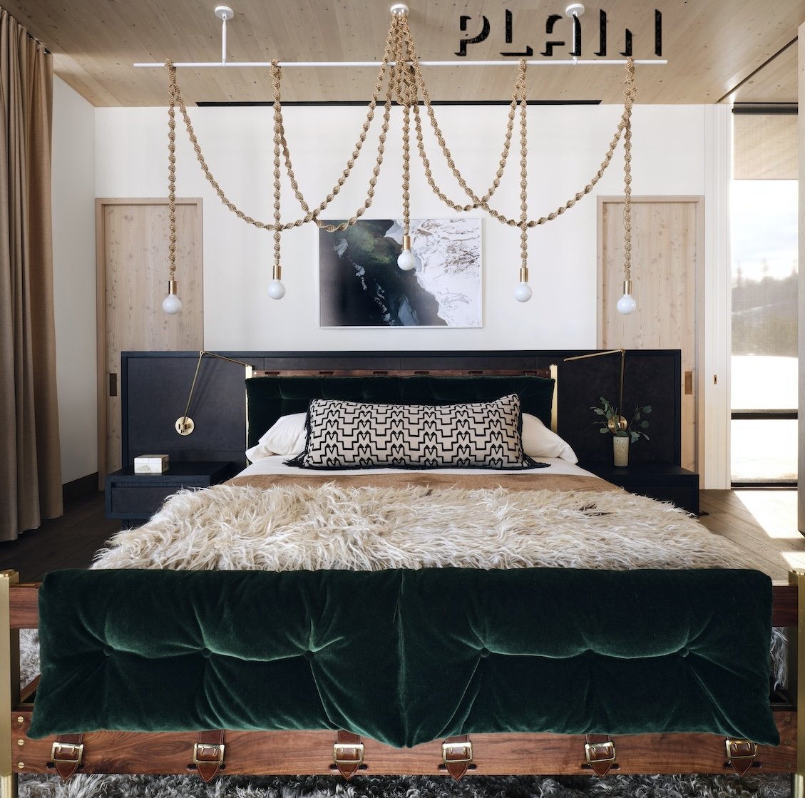 A modern bedroom with a green velvet bed, black nightstands, and a large fluffy beige rug. Hanging from the ceiling is Brightbound Tini Helix chandelier lighting, featuring a Tala bulb and Sunbrella Rope.
