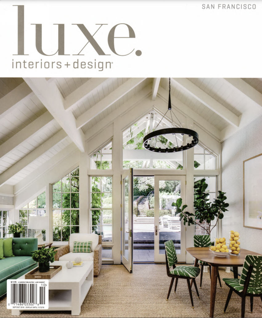 Cover of Luxe magazine featuring a bright, airy living room with large windows, white vaulted ceiling, green and white furniture, and a dining area with a round table and chairs with scroll patterns, and green potted plants.