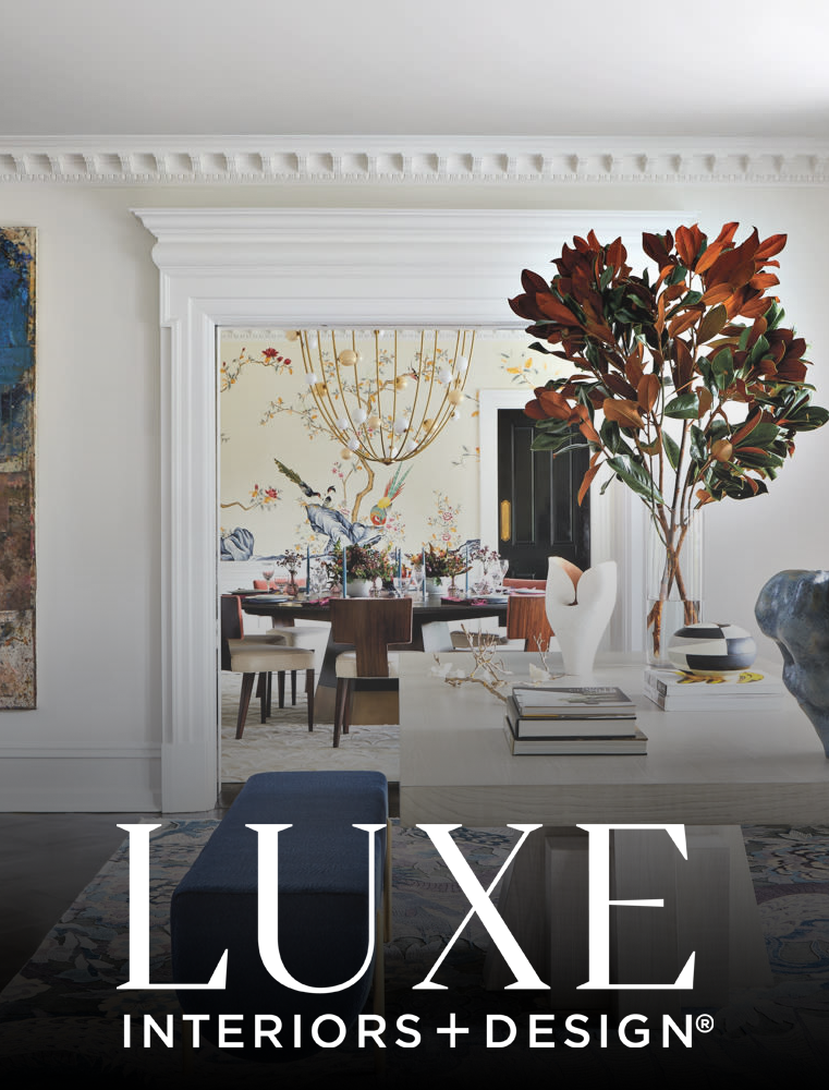 Elegant dining room with a large round table set for a meal, decorated with floral centerpieces, surrounded by wooden chairs, and a colorful wallpaper mural featuring a bird and floral motifs in the background. A white console table in the foreground