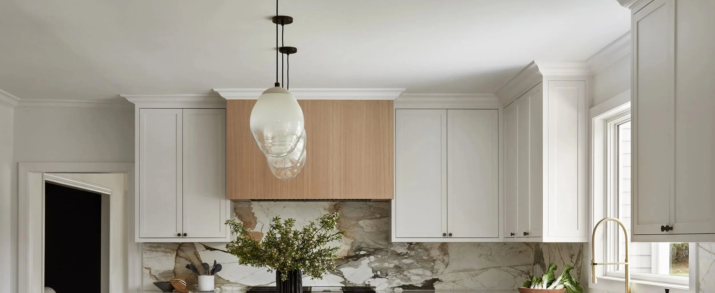 Modern kitchen with white cabinets, marble backsplash, a window, and a brass faucet.