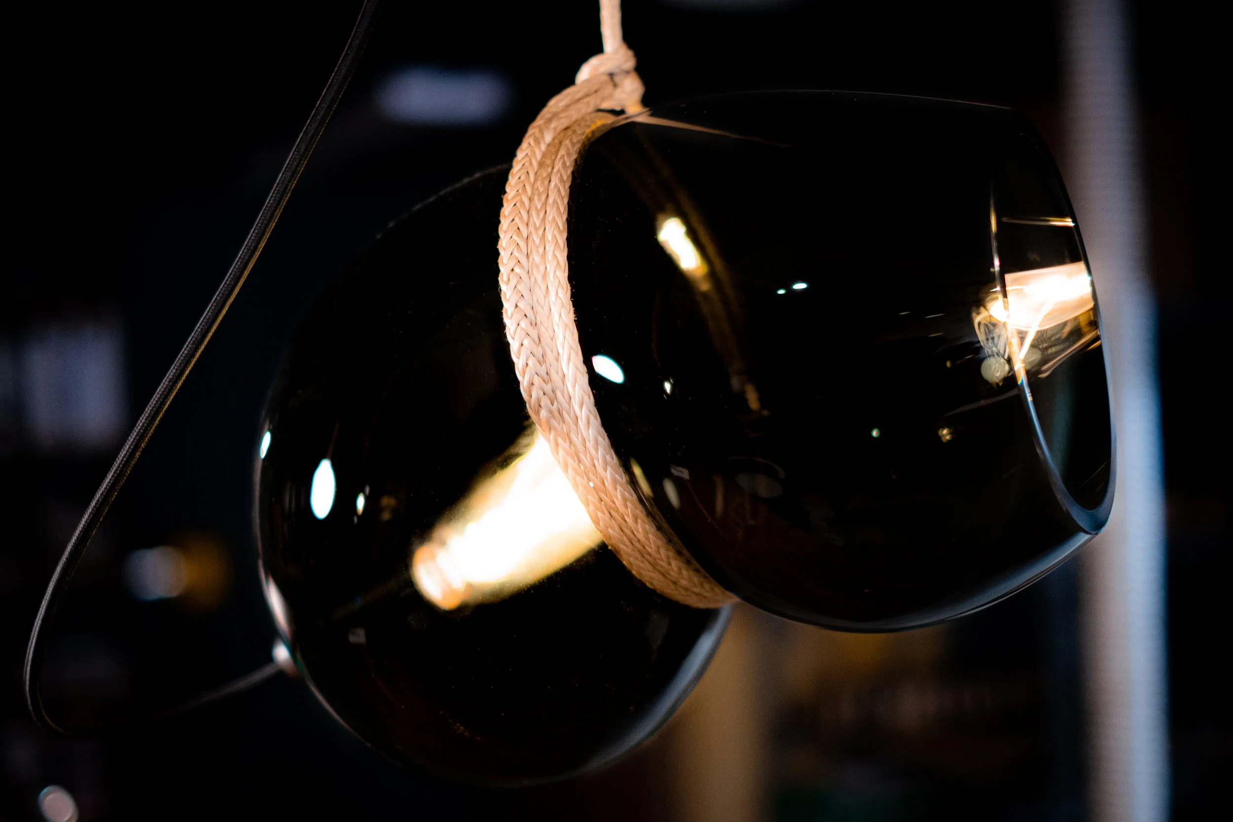 A black spherical object with a light reflection, suspended by a beige woven rope in a dark environment.