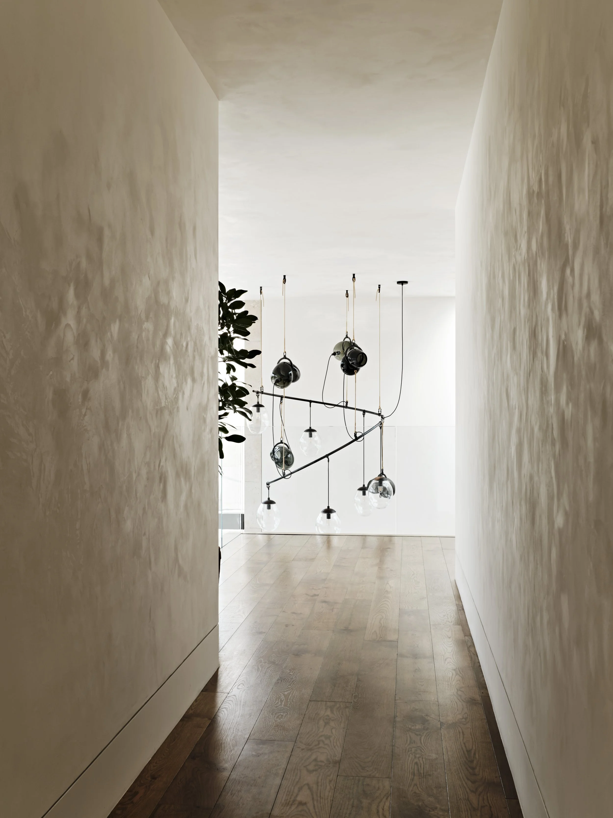 Elegant wine cellar with Gemma studio-blown glass lighting chandelier, a round reflective table in the center, and shelves filled with wine bottles on either side, with a seating area visible through a doorway in the background.