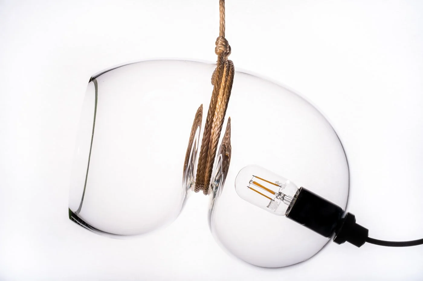 A broken light bulb with a filament, with a frayed electrical cord hanging from the top, and the filament resting on the broken glass edges.
