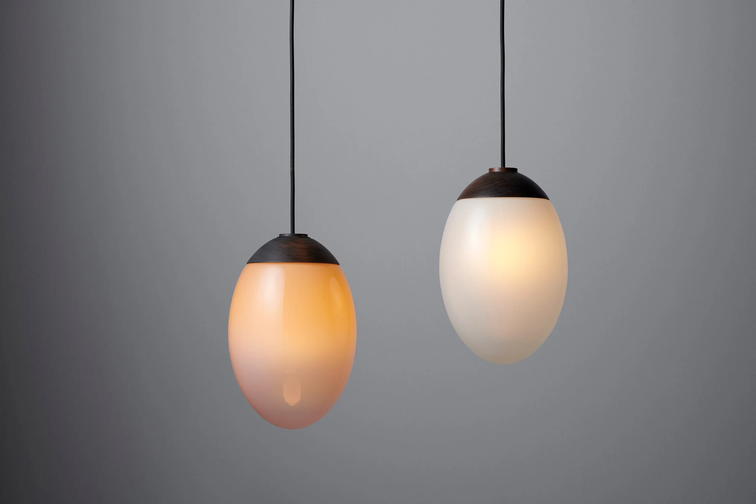 Two hanging pendant lights with oval-shaped frosted glass shades and dark brown tops, against a plain gray background.