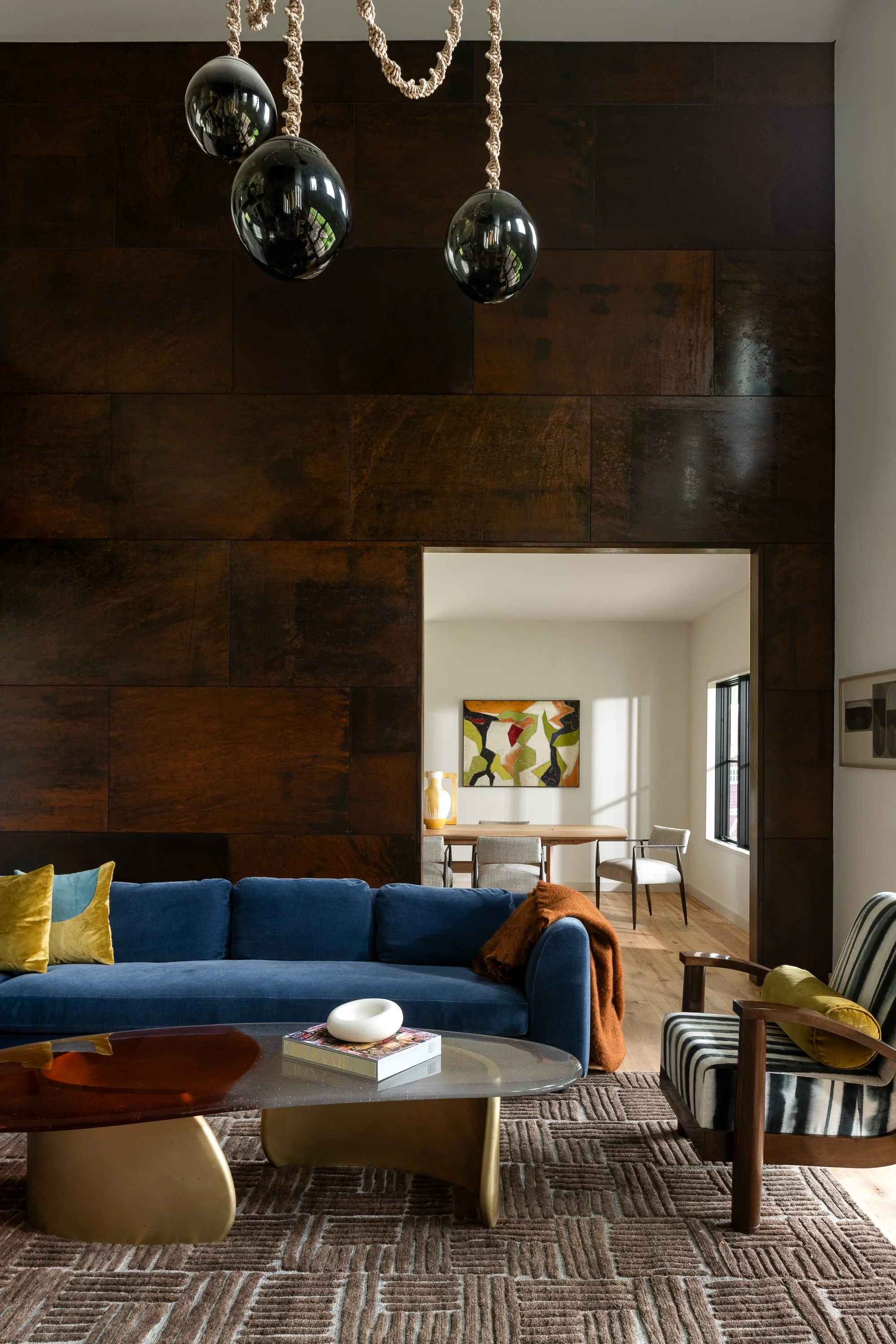 Living room with blue sofa, striped armchair, coffee table, wall art, and wooden panel wall