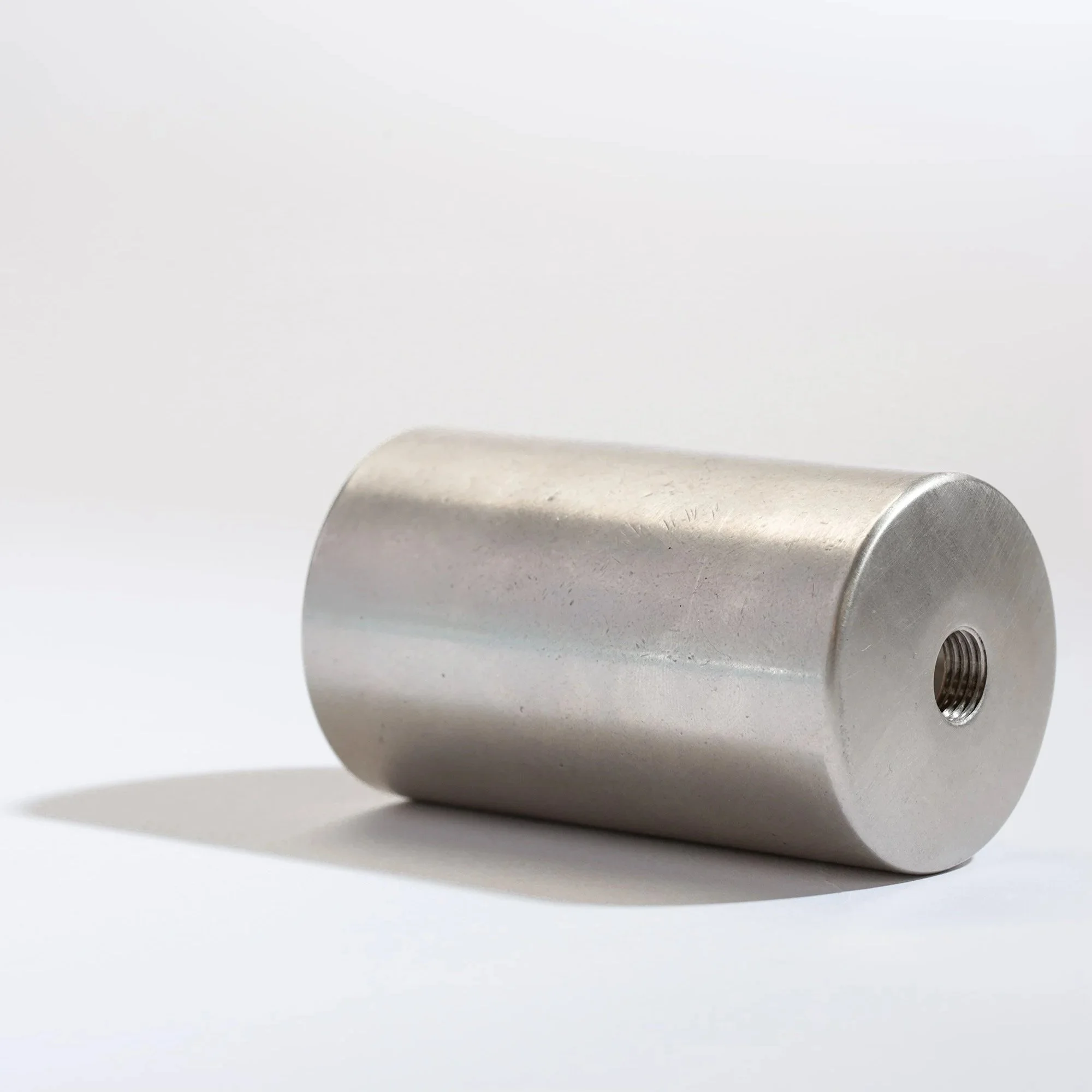 A cylindrical metal object with a threaded hole on one end, placed on a white surface.