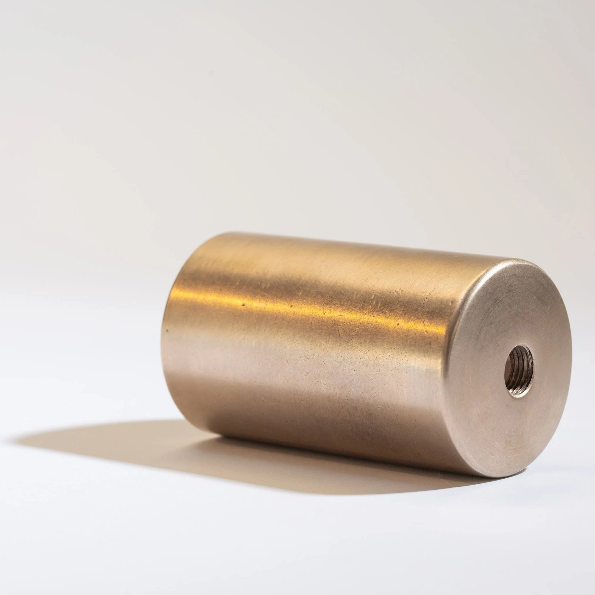A metallic cylindrical object lying on a flat surface with a hole on one end, casting a shadow.