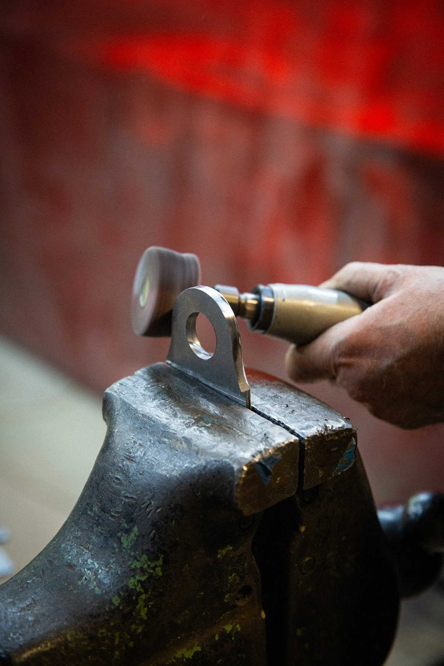 A person using a rotary tool to polish or grind a small metal piece held in a bench vise.