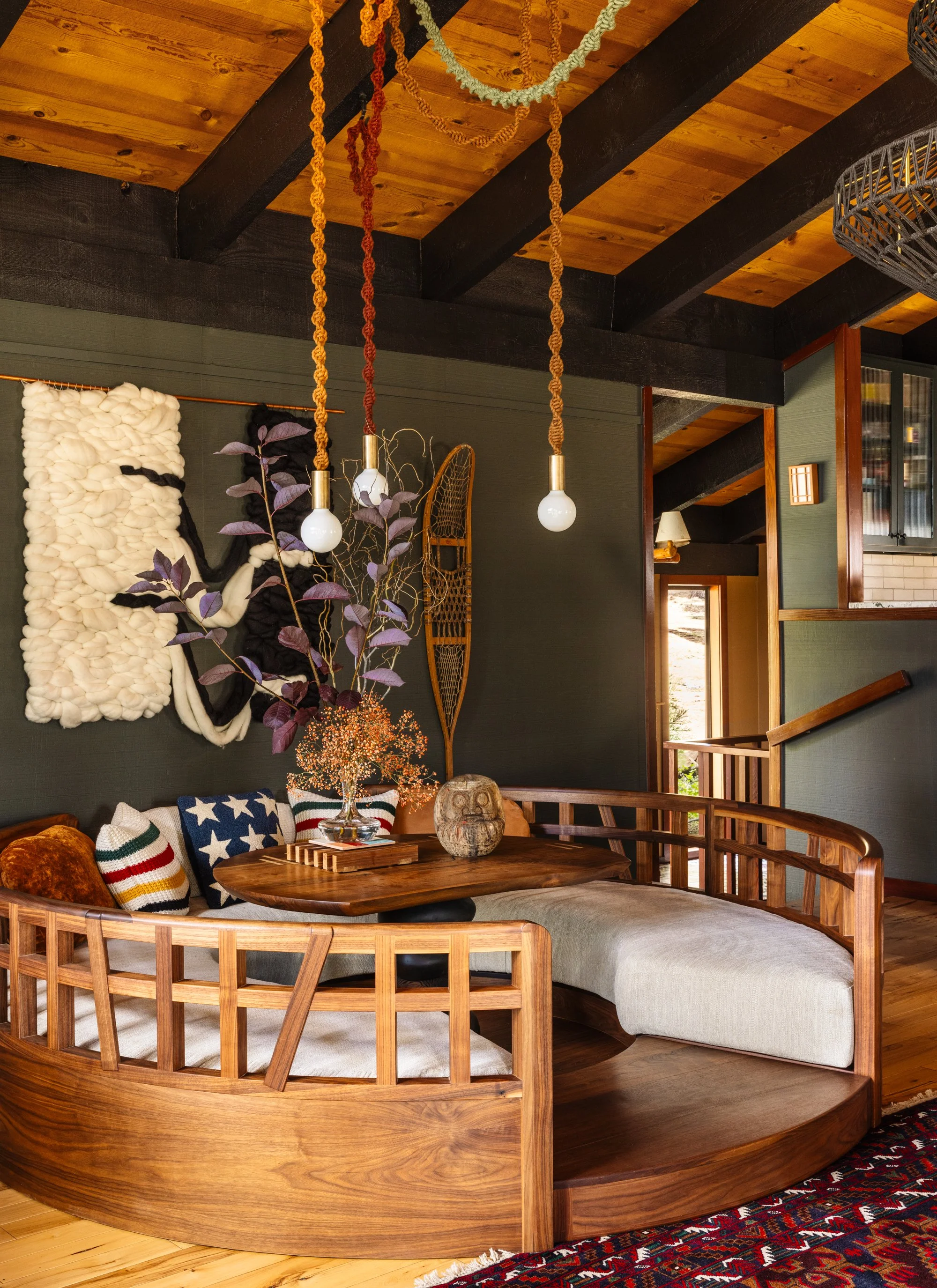 Modern dining room with a large marble table, 10 upholstered chairs, wooden beams, floor-to-ceiling windows with mountain and forest view, and TwentyTwo Brightbound studio-blown architectural lighting fixture.