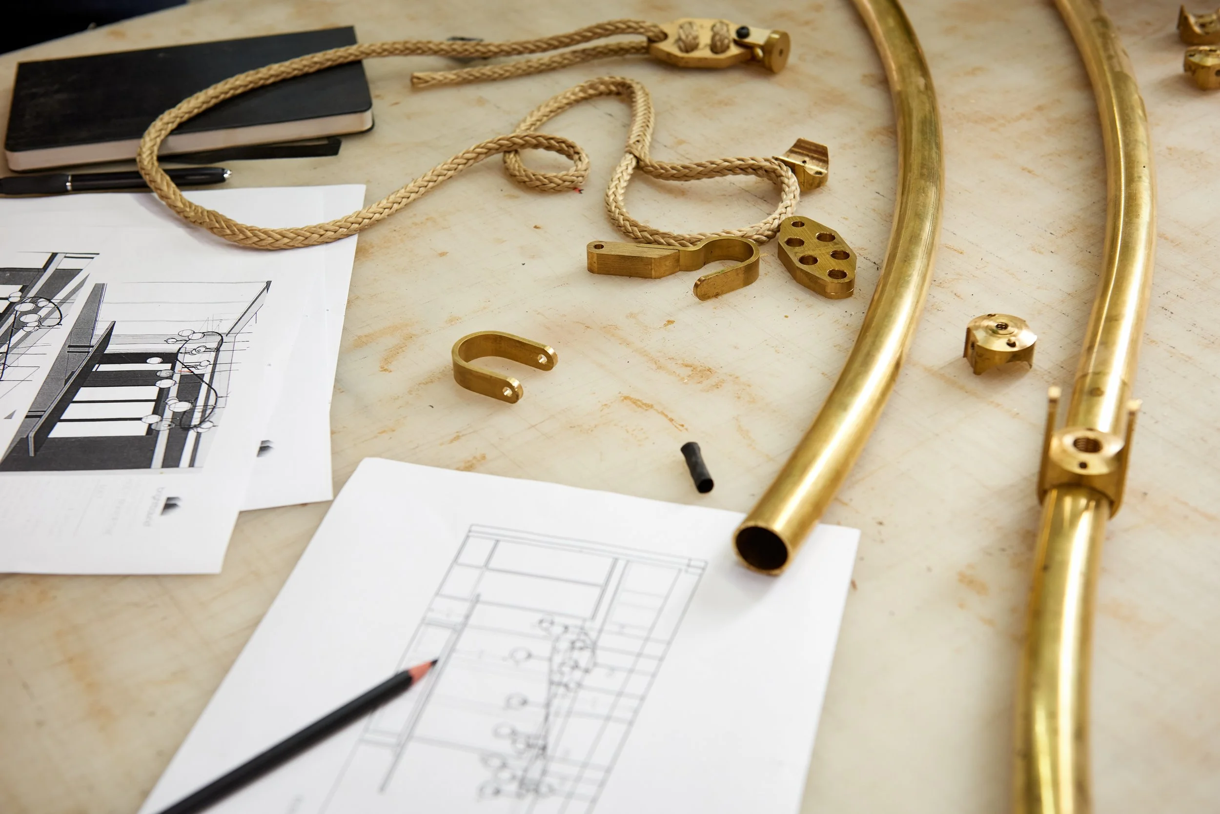 Disassembled brass and gold-colored musical instrument parts with sketches and notes on a work table.