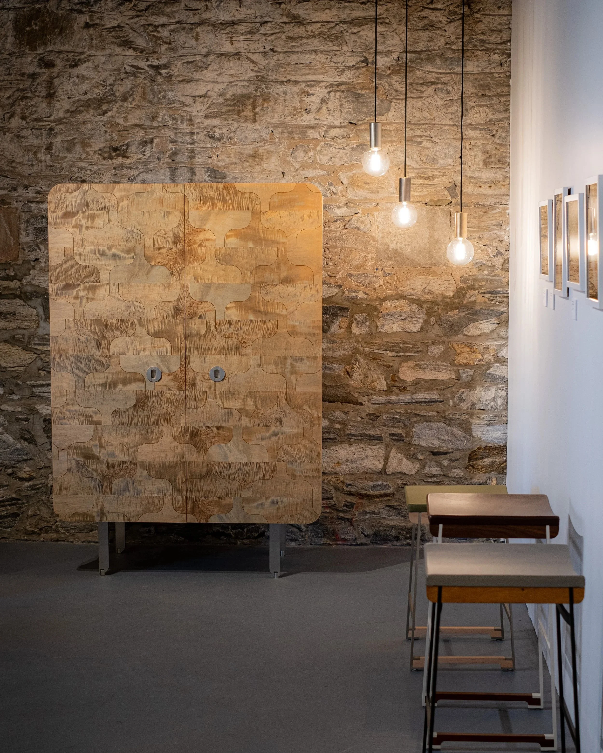 A modern interior with a textured stone wall, wooden cabinet, hanging light bulbs, and a white wall with framed pictures.